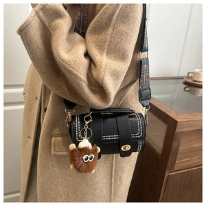 Detail of black cylinder crossbody bag with vintage blue strap and brown plush charm