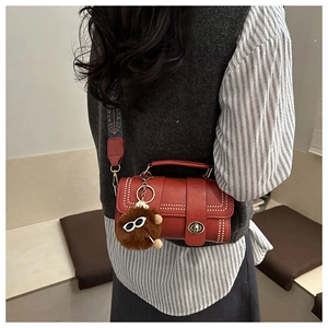 Detail of red lychee grain leather Boston bag with lion charm and wide ethnic strap