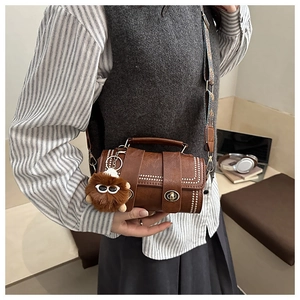Brown cylinder Boston bag featuring white studs and a plush monster charm with wide strap