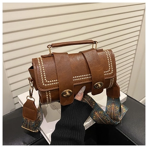 Detail of vintage brown cylinder bag with gold rivets and colorful jacquard strap
