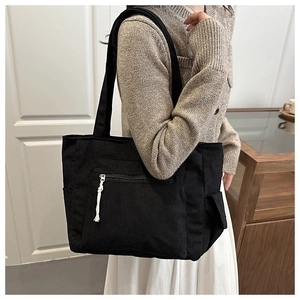 Detail of black corduroy tote bag with side pocket and knot zipper on shoulder