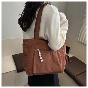 Detail of a brown corduroy tote bag showing textured side pocket and zipper with cord charm