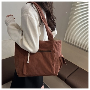 Detail of brown corduroy tote bag showing front zipper pocket and side slot compartment