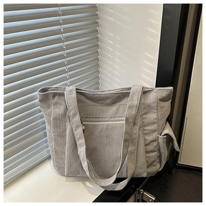 Detail of grey corduroy tote bag showing front zipper pocket and side open pocket