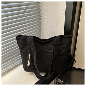 Detail of black corduroy tote bag featuring a front zipper pocket and white tassel accents