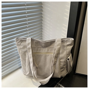 Detail of grey corduroy tote bag showing front zipper pocket and side button compartment