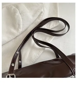 Detail of dark brown leather shoulder bag featuring metal eyelets and slender strap handles