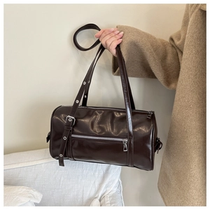 Detail of dark brown cylinder bag showing glossy leather texture and silver zipper pocket