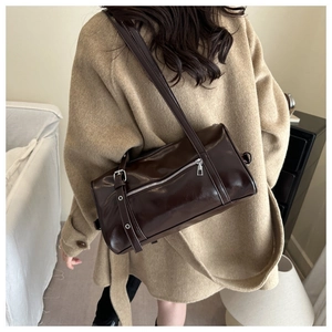 Detail of a dark brown barrel shoulder bag with glossy leather and silver hardware