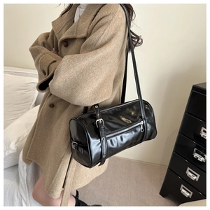Detailed view of black glossy pillow bag with silver hardware on a model shoulder