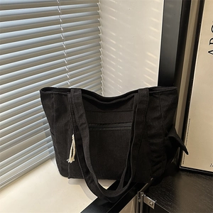 Black corduroy tote bag with dual straps and zipper pocket in a minimalist interior setting