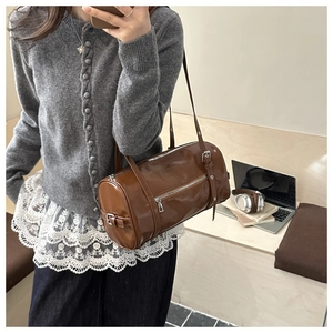 Close-up of a brown leather cylinder bag shown in a stylish lifestyle commuting setting