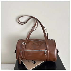 Detail of brown glossy cylindrical pillow bag with silver zippers and adjustable strap