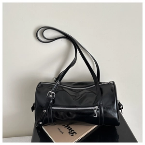 Detail of black glossy cylindrical pillow bag with silver hardware on magazine background