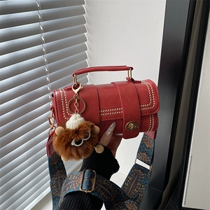 Detail of red pebbled leather handbag with gold studs, print strap and furry charm