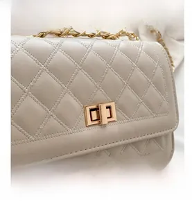 Detail of beige quilted shoulder bag with gold twist lock and metal chain strap