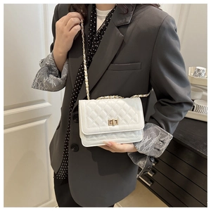 Detail of white quilted crossbody bag featuring golden chain strap and turn-lock closure
