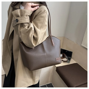 Close-up of brown lychee grain leather tote bag with fashion label on khaki trench coat