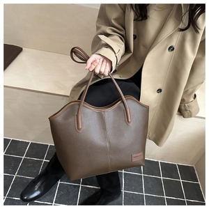 Detail of vintage dark brown tote bag with pebbled leather texture and letter plaque