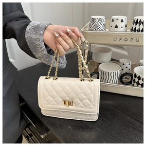 Macro detail of beige quilted crossbody bag with golden twist lock and chain strap