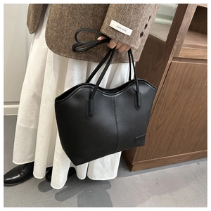 Detail of black lychee grain leather tote bag showing smooth texture and brand plaque
