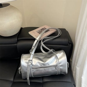 Metallic silver cylinder shoulder bag with adjustable straps on a minimalist leather bench