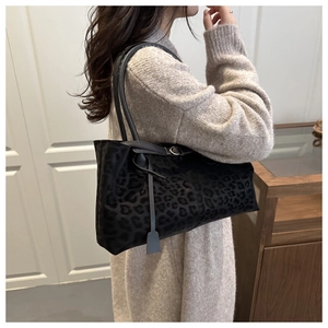 Detail of black leopard print suede shoulder bag with leather strap on a model