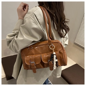 Braune glänzende Boston-Tasche mit Außentaschen und Perlenanhänger am Model