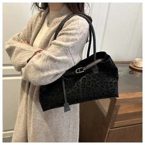 Close-up of black leopard print suede tote bag worn over shoulder in a cafe setting