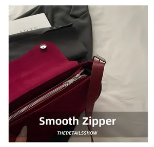 Detail of smooth silver zipper and magnetic clasp on a dark red suede shoulder bag