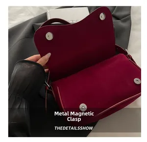 Close-up of metal magnetic buckle and matte suede texture on burgundy underarm bag