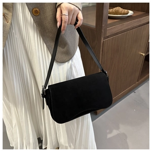 Close-up of black matte suede shoulder bag with adjustable strap worn on a brown blazer