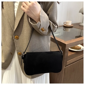 Close-up of matte black underarm bag with minimalist shoulder strap in a cafe setting