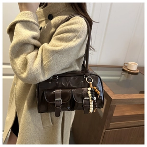 Detail der dunkelbraunen Boston-Tasche aus Lackleder mit Perlenanhänger und Gürtelschnallen