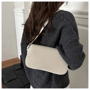 Detail of a beige underarm bag featuring a unique wavy flap and matte leather texture
