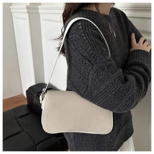 Detail showing the curved wave bottom and matte leather texture of the ivory underarm bag