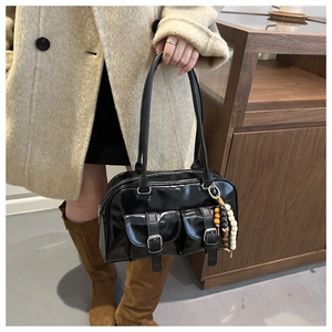 Detail einer glänzenden schwarzen Boston Bag mit zwei Fronttaschen und Holzperlen-Anhänger