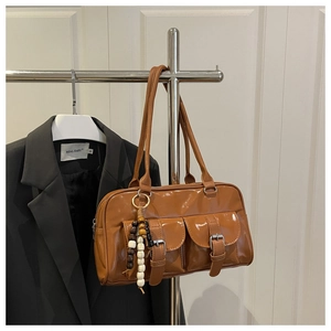 Detail einer braunen glänzenden Boston Bag mit Schnallentaschen und Holzperlenanhänger