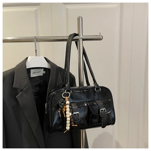Detail einer schwarzen Lackleder-Boston-Tasche mit Schnallentaschen und Perlenanhänger