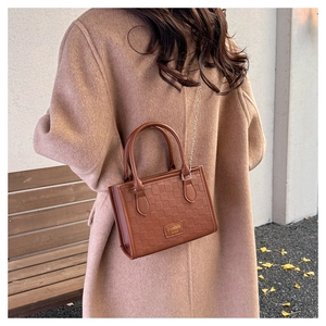 Détail du sac marron à texture damier avec emblème doré et chaîne métallique