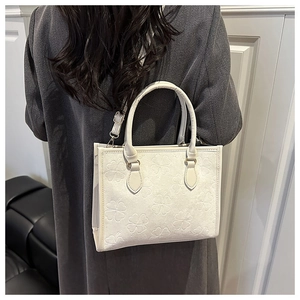 Close-up of off-white tote bag featuring embossed clover patterns and stylish shoulder strap