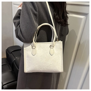 Close-up of stylish cream-colored handbag featuring detailed four-leaf clover embossing