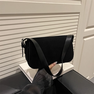 Minimalist black suede underarm saddle bag with wide strap on white background