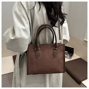 Macro detail of brown suede tote with embossed clover patterns and leather handles