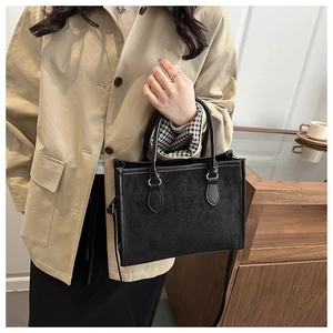Detail of clover embossed leather tote bag shown on a model in a trench coat