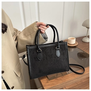 Detail of clover embossed matte black handbag held by model in a cozy lifestyle setting