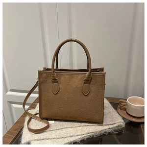 Detail of brown clover-embossed suede tote bag with top handles and slender shoulder strap