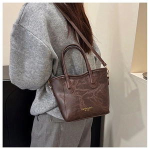 Detail of dark brown pleated leather bucket bag worn as a crossbody by model