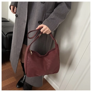 Detail view of burgundy crescent tote bag with adjustable strap worn on wool coat