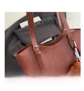 Dettaglio borsa tote in pelle marrone con ciondolo a orsetto e foulard di seta